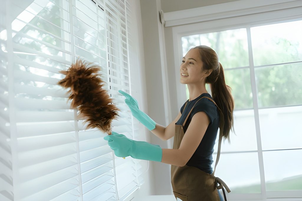 Professional maid dusting window blinds during home cleaning in Dubai